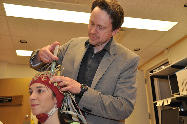 SFU psychologist John McDonald demonstrates how conductive gel is injected into sensors worn by SFU first year master's student Ashley Livingstone. The gel allows electrical fields to flow from Livingstone's brain into the researchers' recording apparatus.